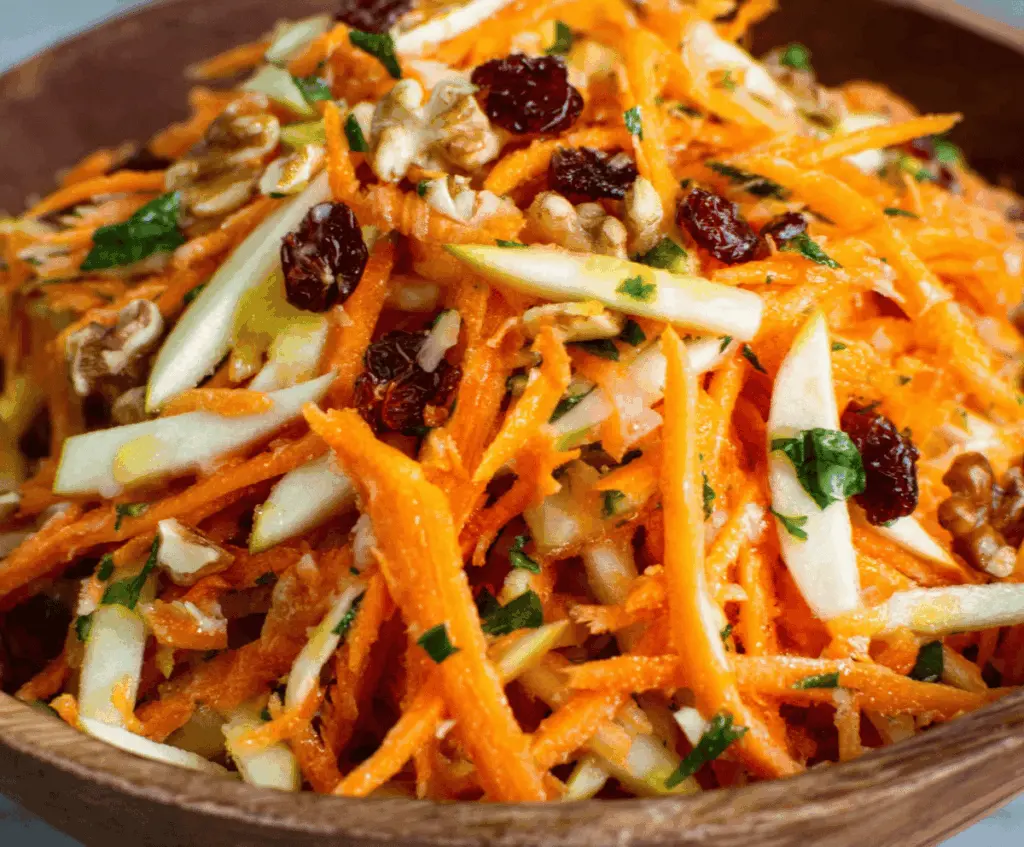 Fresh carrot and apple salad in a glass bowl, featuring vibrant orange and red colors with shredded carrots and crisp apple slices, perfect for a healthy snack or side dish.