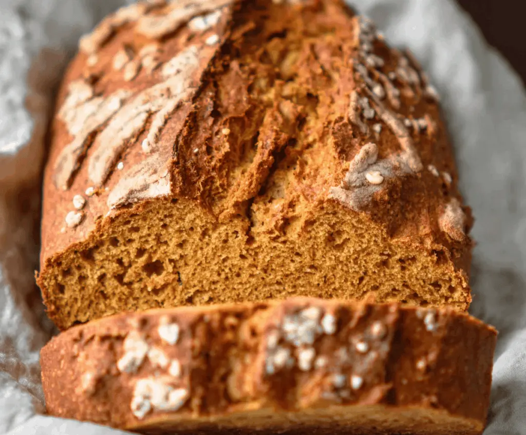 Freshly baked pumpkin sourdough bread with a golden crust and soft interior, garnished with pumpkin seeds, on a rustic wooden surface.
