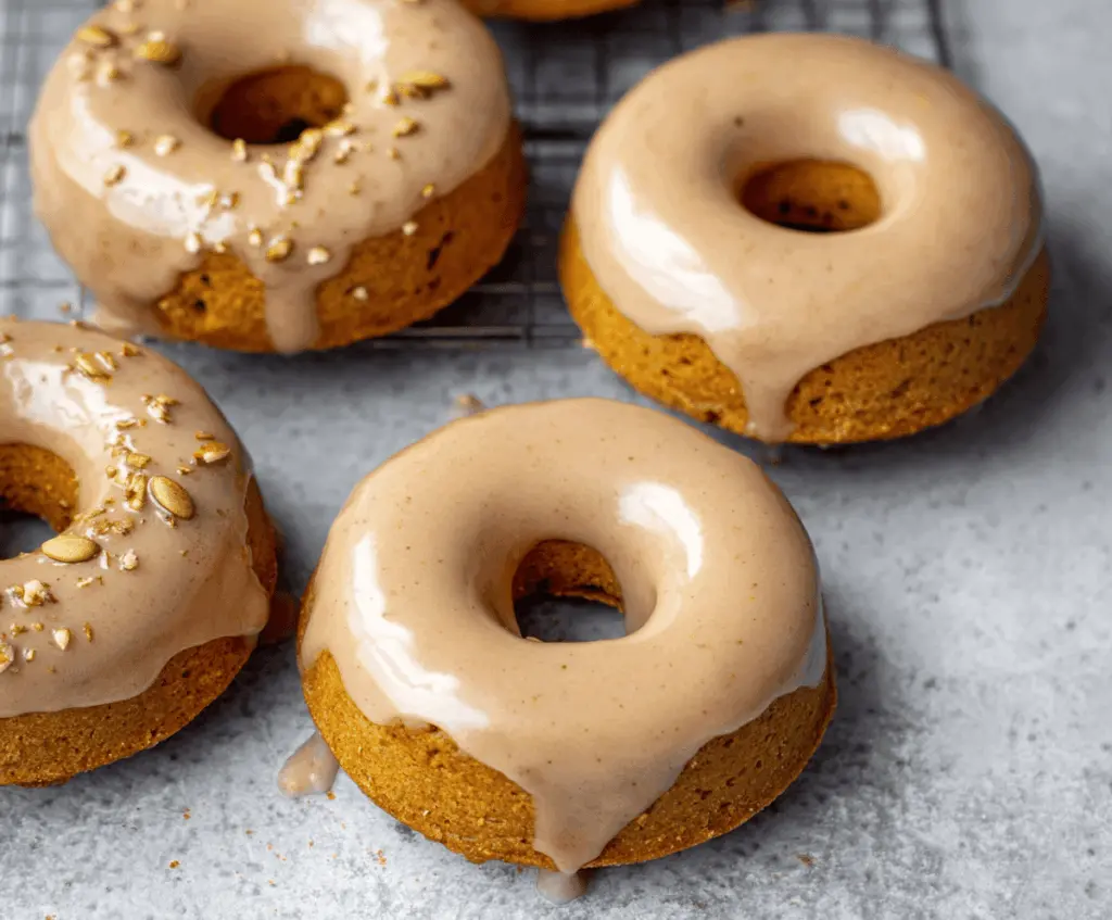 Delicious baked pumpkin donuts topped with glossy maple glaze on a rustic wooden surface