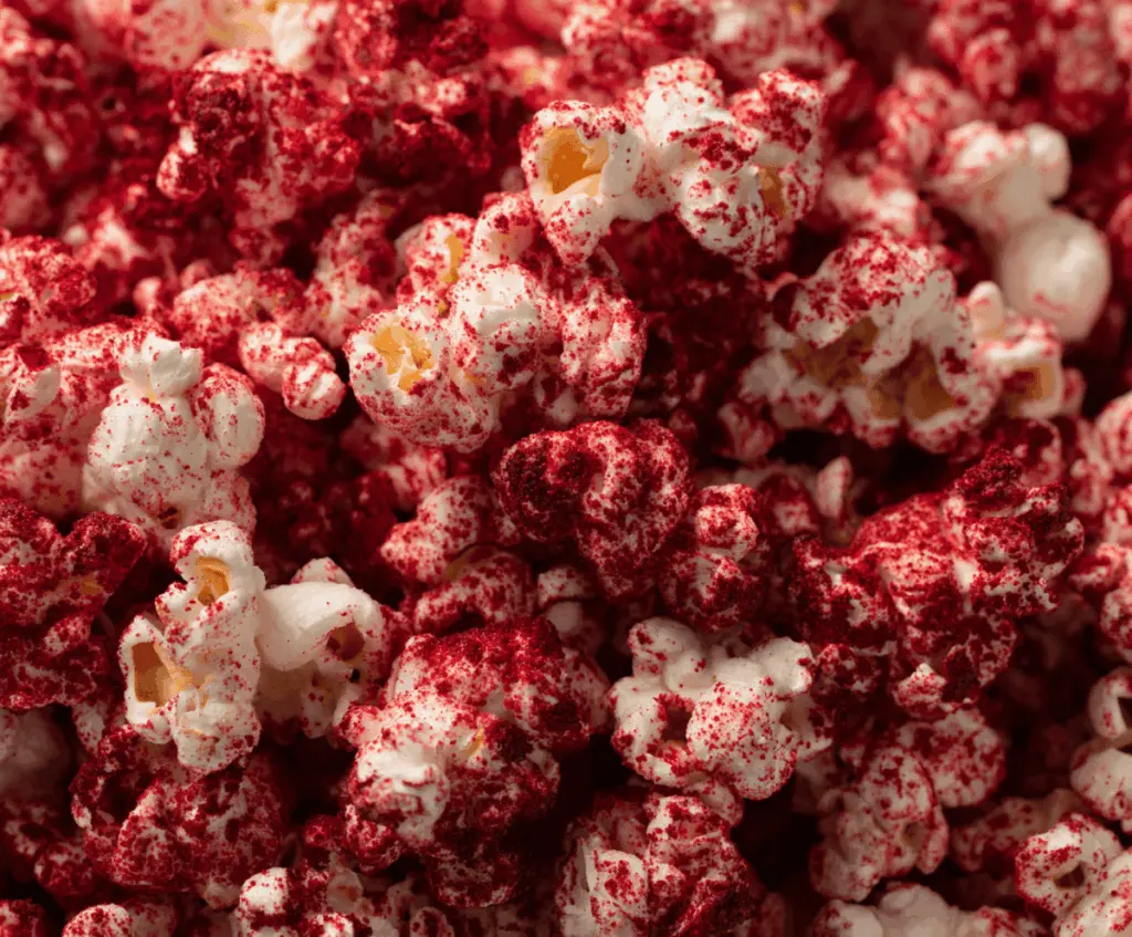 Bright red velvet popcorn topped with creamy frosting and red sprinkles, perfect for a spooky party snack.