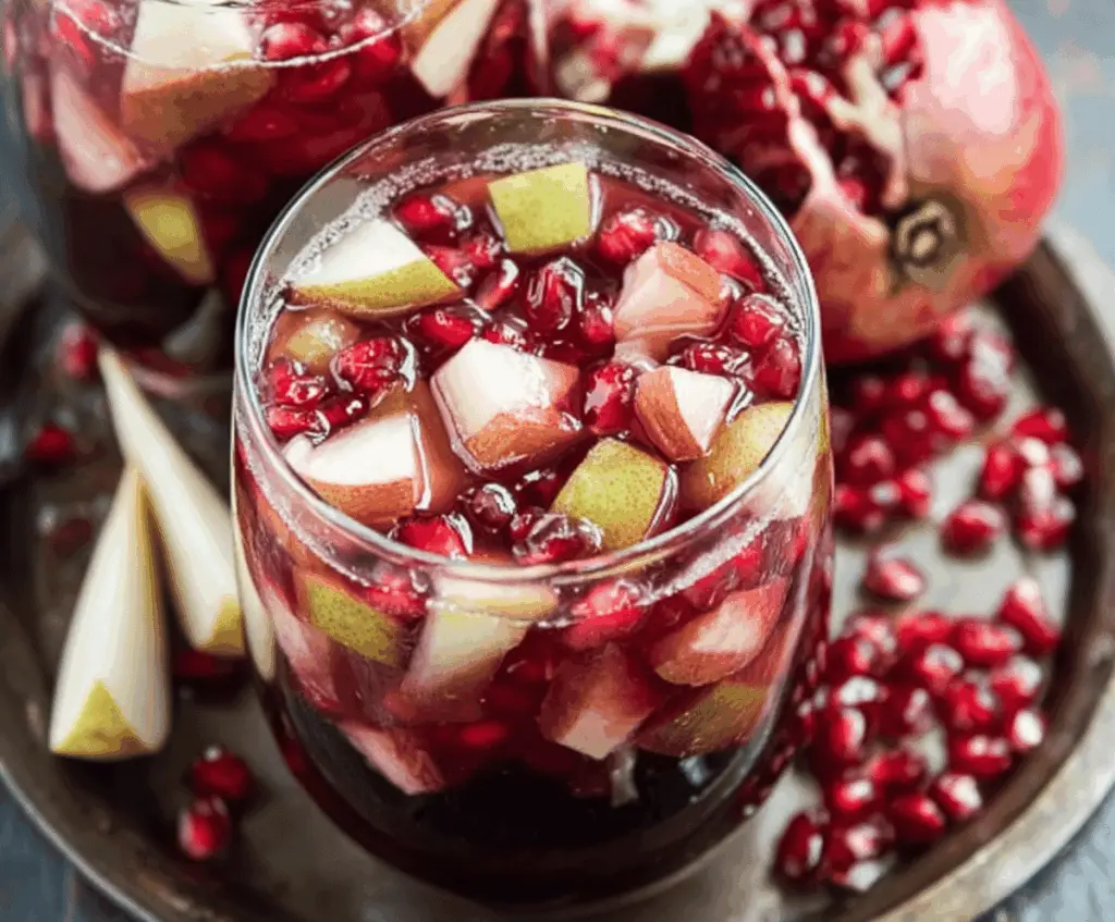 Refreshing Harvest Sangria featuring Pomegranate and Pears, garnished with fresh fruit slices in a glass pitcher