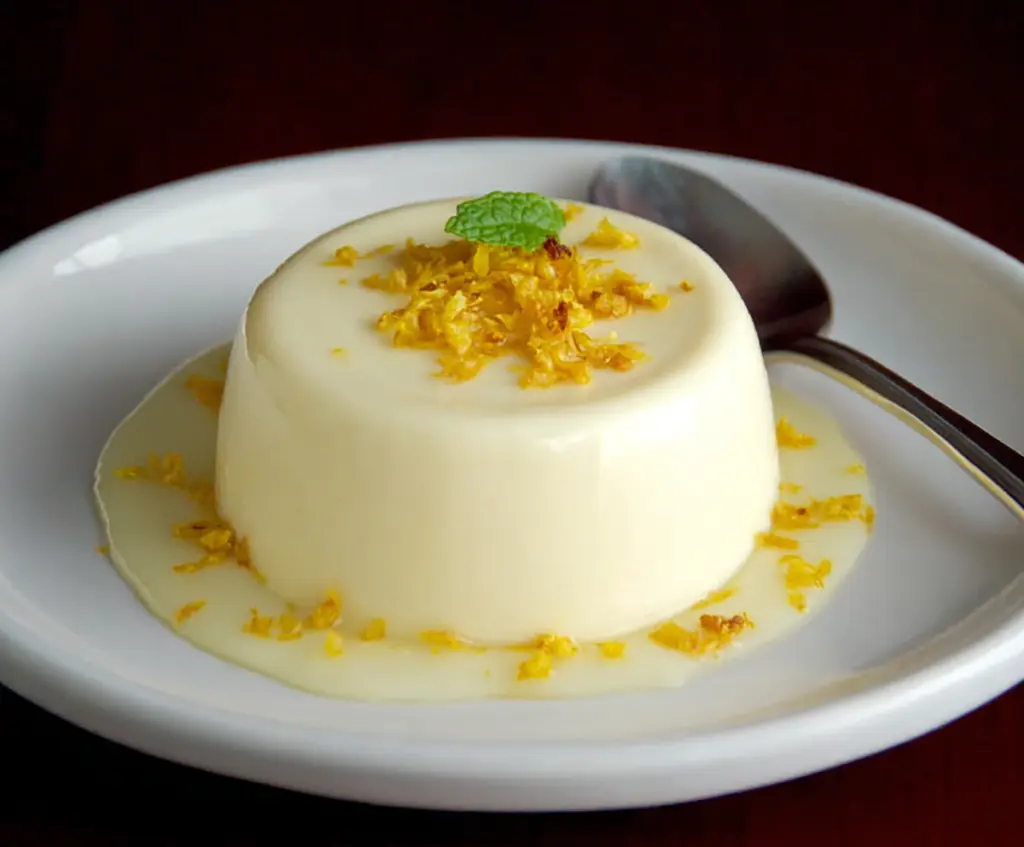 Creamy Lemon Panna Cotta served in a glass with lemon zest and berries on top.